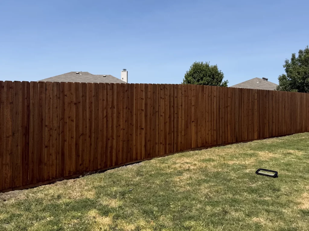 Finished cedar fence after replacement in Arlington, TX with medium brown stain along the property line