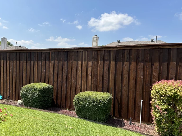Finished 8 ft cedar fence in Mansfield, TX running behind established landscaping in a residential backyard