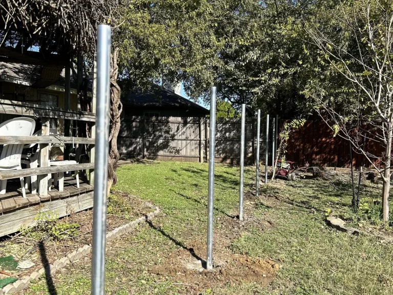 Galvanized steel fence posts set in concrete along the line before cedar pickets go up in Arlington, TX