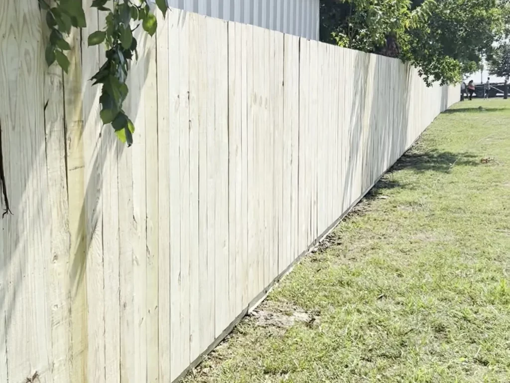 Finished pressure treated fence in Venus, TX running 250 feet along a property line beside a metal building