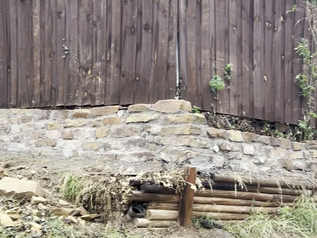 Sandstone courses laid over the old timber wall during retaining wall construction in Haltom City, TX