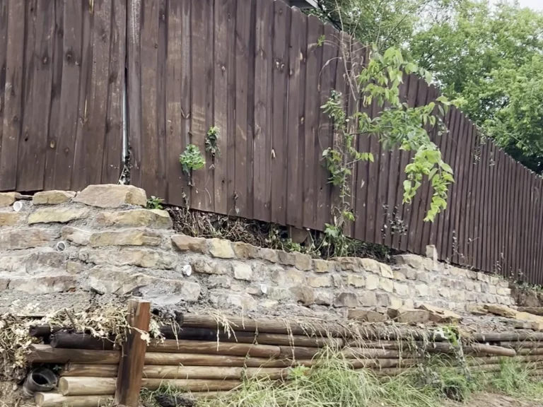 New sandstone retaining wall in Haltom City, TX built along a slope beneath an existing wood fence