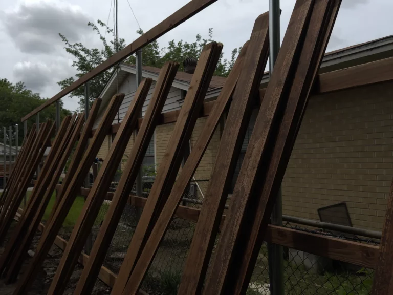 Stained 1x6 cedar pickets staged along the old chain-link line during a fence installation in Grand Prairie, TX